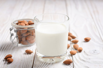Milk or yogurt in drinking glass on white wooden table with almonds in airtight conainer aside