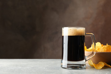 Glass of dark beer and chips on grey table, space for text