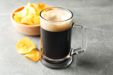 Glass of dark beer and chips on grey background, space for text