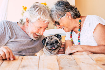 People and dog concept with couple of happy couple of senior mature man and woman smiling and having fun with their little puppy pug  - concept of animal therapy and happiness