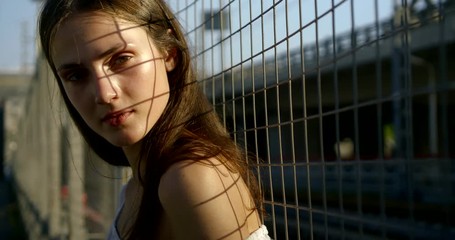 long haired brunette stands in metal grid shadow closeup