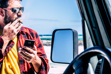 Handsome standing man with cigar use mobile   phone outside his black car - beach and ocean in background for travel and adventure lifestyle concept -  people in outdoor leisure activity
