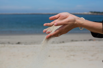 Fototapeta na wymiar Sand pours through fingers against the Ocean.