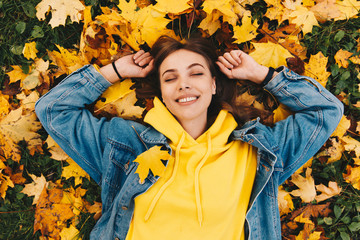 Autumn walk. Woman portrait. Happy girl in yellow hoodie and jean jacket is smiling while lying...