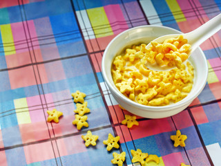 Easy Food, Breakfast cereal with stars shapes, In a white cup with milk inside, On a multicolored plaid tablecloth.