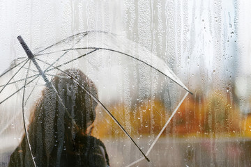 A woman silhouette with transparent umbrella through wet window with drops of rain. Autumn © flowertiare
