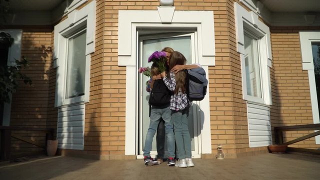Little cute boy and girl with backpacks coming home and bringing flowers for their mother. Happy loving family concept