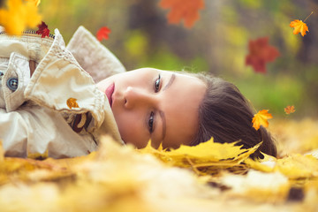 Portrait of sad beautiful young woman lying on the ground of an autumn forest with colorful maple leaves. Concept