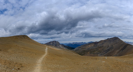 Hiking trail through a panoramic Rocky Mountain landscape with a white clouds, mountains and hills.