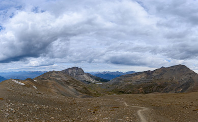 Hiking trail through a panoramic Rocky Mountain landscape with a white clouds, mountains and hills.