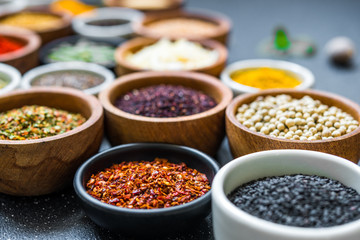 Variety of colorful spices, herbs, and seeds on black stone background