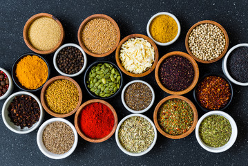 Variety of colorful spices, herbs, and seeds on black stone background