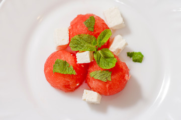 Salad of watermelon balls, feta cheese and mint, sprinkled with sesame seeds in a white plate. Close up