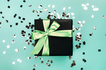 Black gift box with mint bow on turquoise background with glitter. Holiday concept.