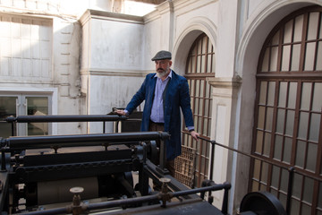 Obraz na płótnie Canvas Worker standing on top platform of an old vintage press for newspaper printing