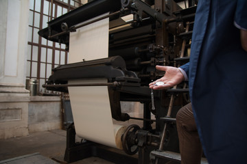 Human hand holding vintage pocket watch in front of an old printing press