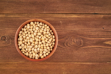 Dried chickpea in wooden bowl on brown background, top view, copy space