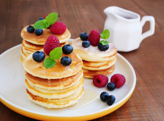 Mini pancakes with raspberries, blueberries and syrup on white plate. Stacks of silver dollar pancakes.