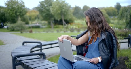 long haired brunette opens modern laptop and types in park