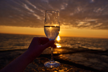 hand holding glass of white wine and with sea and beautiful sunset at background, close-up. Summer evening relaxed mood concept