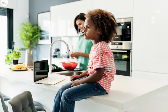 Girl sitting on kitchen counter with laptop and mother in background