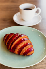 A vertical photo of a croissant with strawberry filling on a bright green plate and a white cup of black coffee.