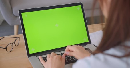 Closeup back view portrait of young caucasian female doctor using laptop with green chroma key screen indoors in office