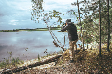 Naklejka premium A man in a gray jacket, take a photo of nature on the banks of the river, in the forest