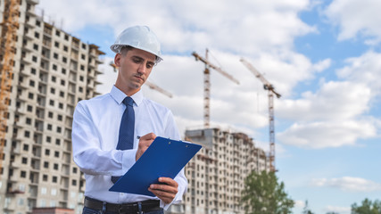 civil engineer in a white helmet makes pencil marks in the documentation.