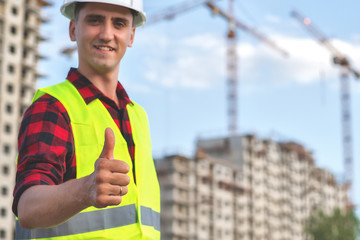 civil engineer in a white helmet on the background of construction, with a raised thumb.