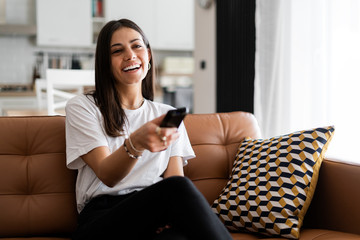 Happy young woman sitting on couch at home watching Tv