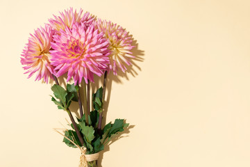 Festive flower bouquet over pastel yellow background, copy space. Top view. Creative greeting card with pink dahlia flowers
