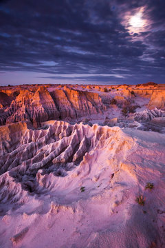 Full moon peeps out of clouds at twilight over eroded Mungo landscape