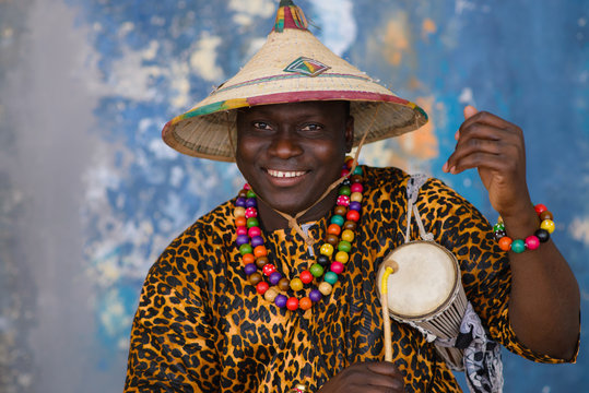 African Man In Traditional Clothes And Fulani Hat Playing On Talking Drum