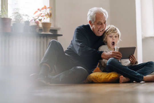 Screaming grandfather and grandson sitting on the floor at home using a tablet