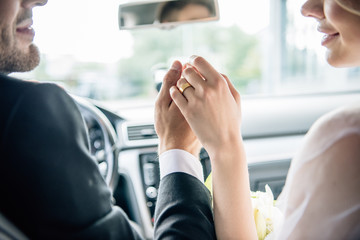 cropped view of bridegroom and bride holding hands in car