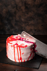 Halloween Bleeding monster cake with a knife on dark background. Red blood on a white cake