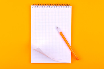 Notebook on a spring with white sheets of paper for drawings, texts and notes, next to a yellow pen lies on an orange background