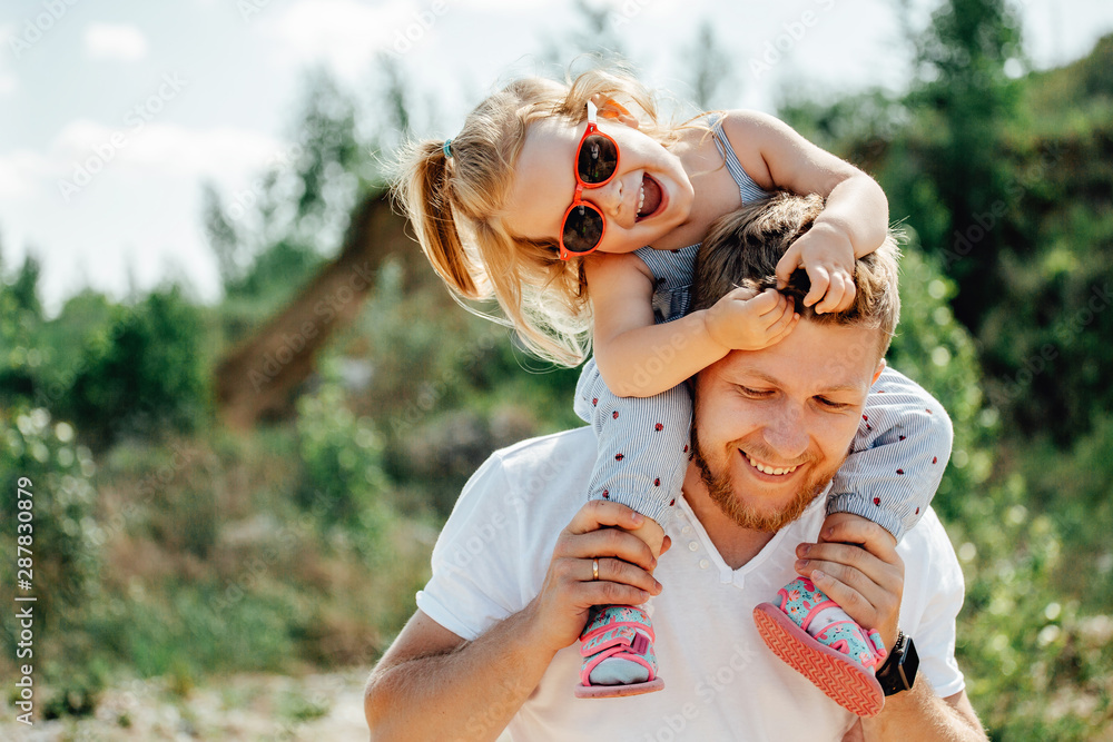 Wall mural little girl sitting on father's shoulders and laughing.