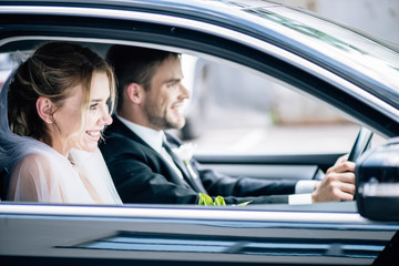 selective focus of attractive bride in bridal veil and bridegroom smiling in car