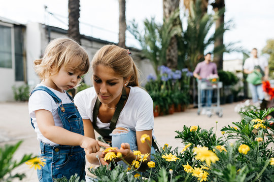 Female worker of a garden center showing flowers to a little girl