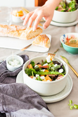 Lunch with green salad with rocket salad, vegetables and goat cheese served  on a beige table with baguette