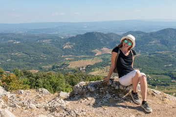 Young independent solo traveler woman sitting and looking at Dentelles de Montmirail mountains,...