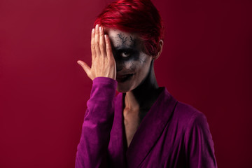 scary clown girl hides half her face behind her hand and smiles creepy