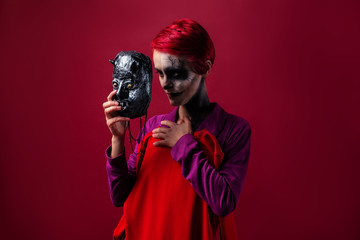 Girl with scary makeup tries on a mask and a red dress