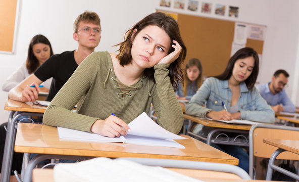 Young Girl Is Writing Test And Thinking About Questions At The Desk