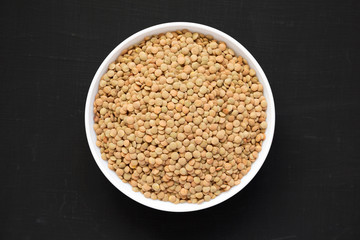 Organic green lentils in a white bowl on a black surface, top view. Flat lay, overhead, from above. Close-up.