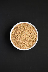 Organic green lentils in a white bowl on a black background, top view. Flat lay, overhead, from above.