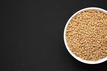 Organic green lentils in a white bowl on a black background, overhead view. Flat lay, top view, from above. Copy space.