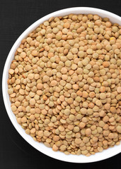 Organic green lentils in a white bowl on a black surface, top view. Flat lay, overhead, from above. Close-up.
